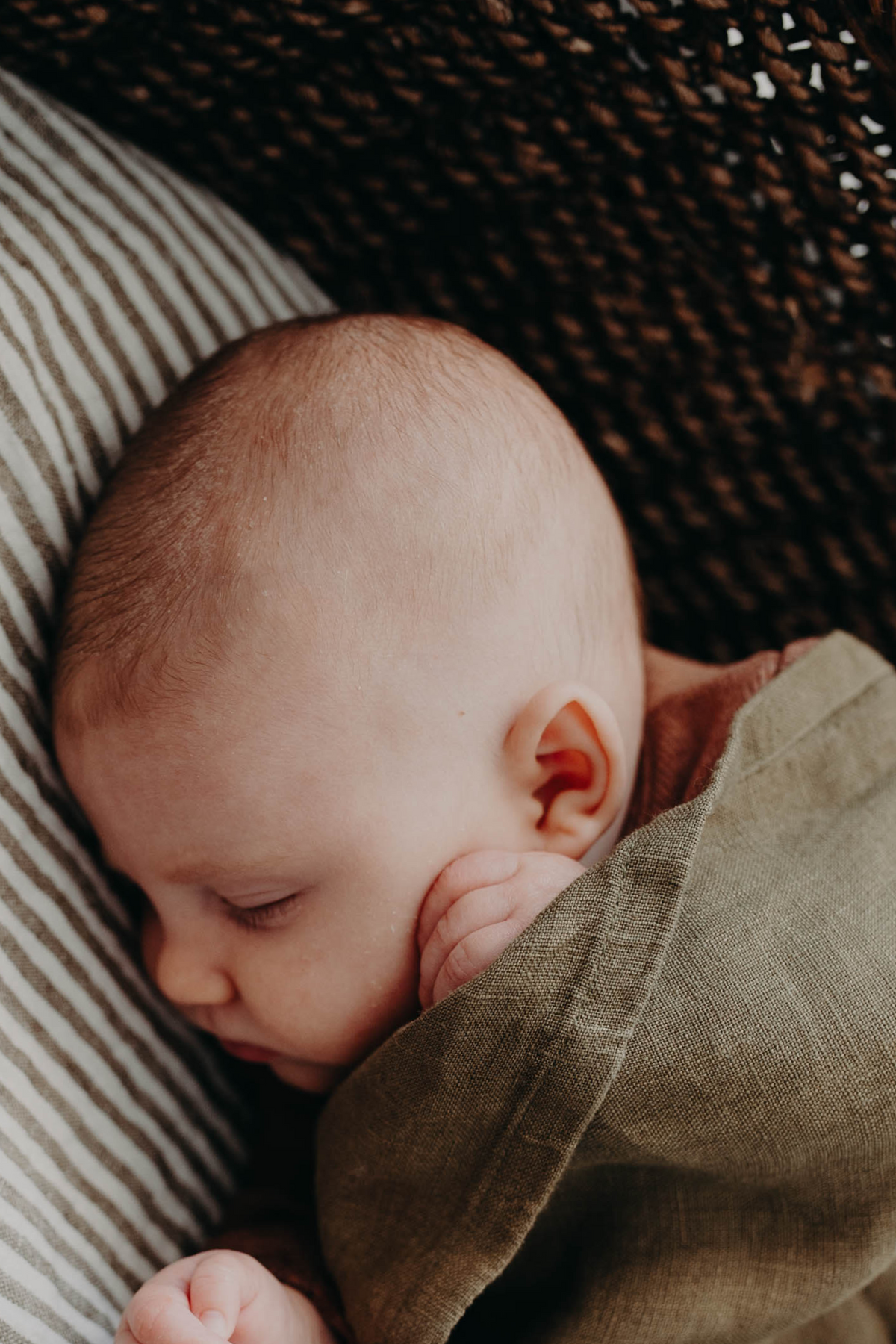 Close on a sleeping newborn's face, wrapped in the Willow linen swaddle on a striped bassinet mattress