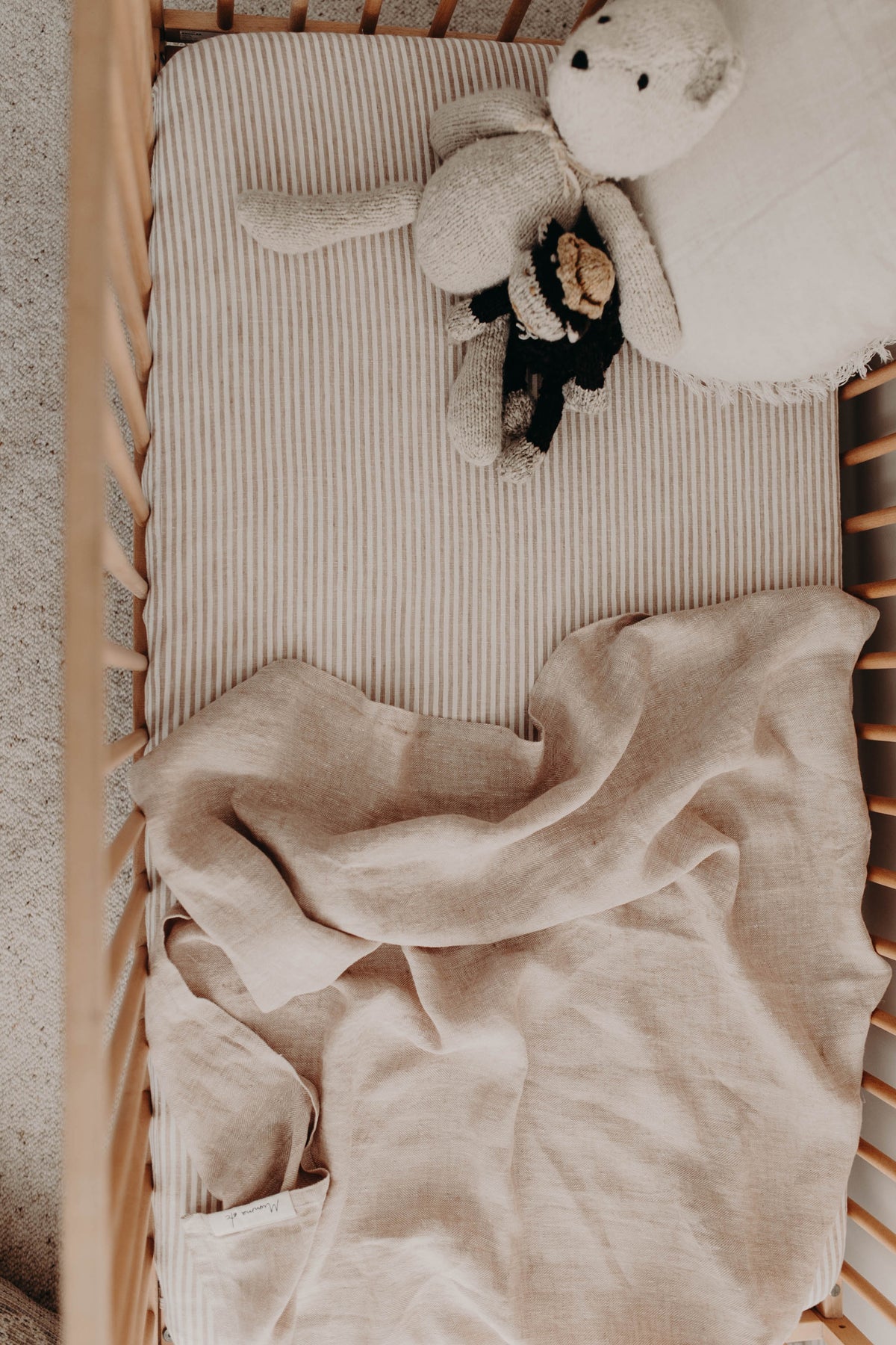 The Meadow linen swaddle unfolded across a cot mattress with a soft toy at the top