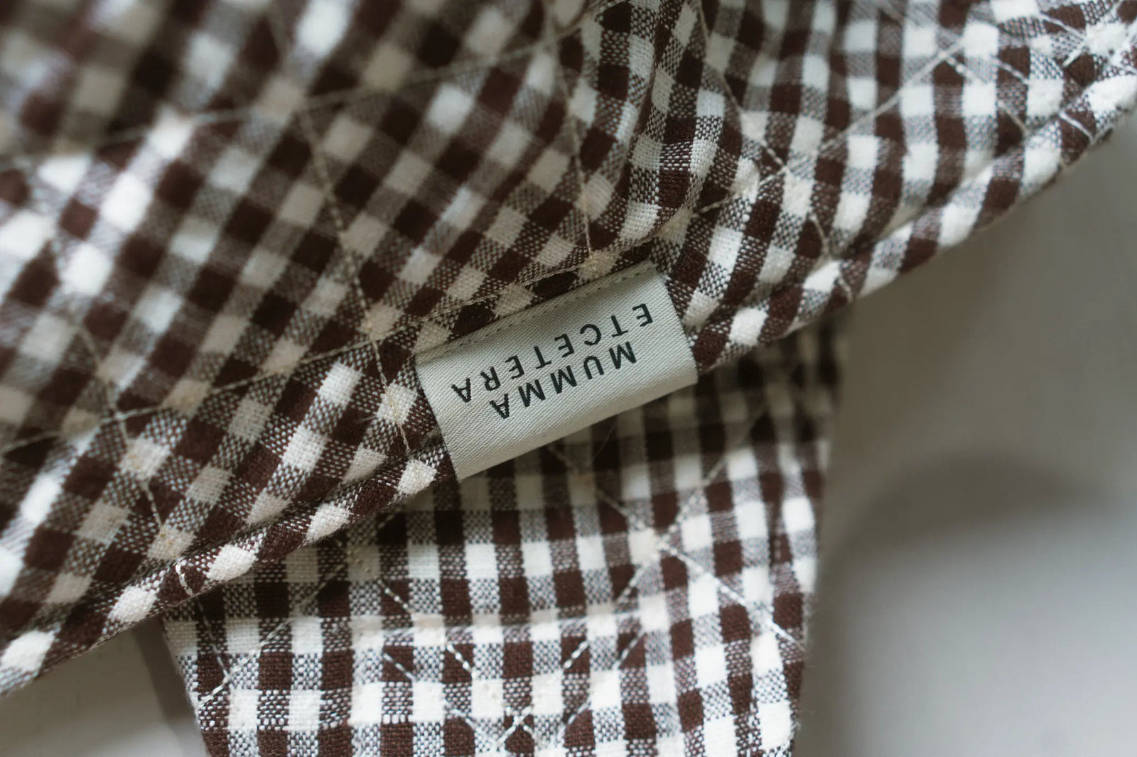The woven Mumma Etcetera label stitched onto quilted chocolate and cream gingham handwoven linen