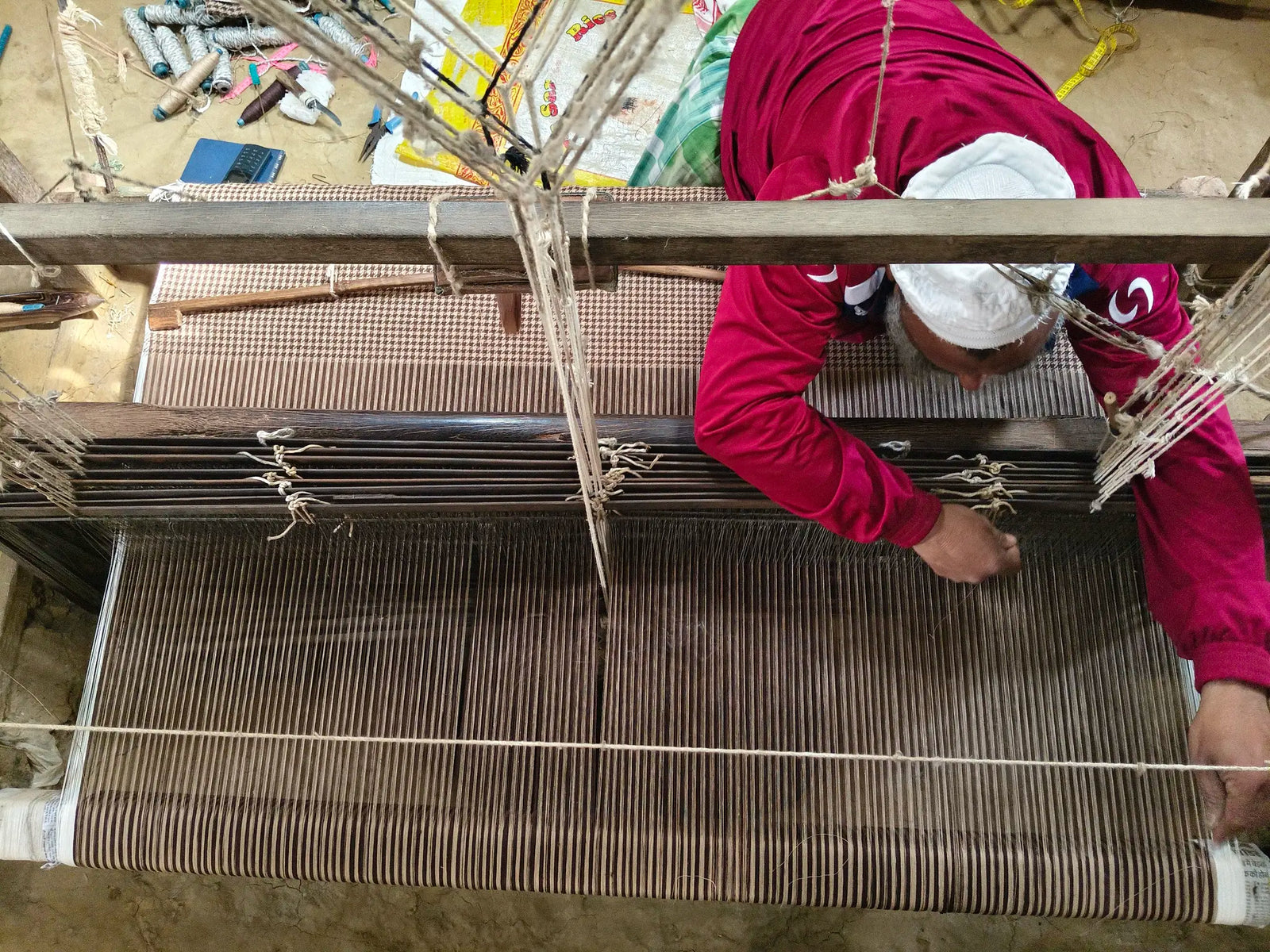 Overhead view of a weaver at a wooden handloom, houndstooth linen taking shape across the warp threads