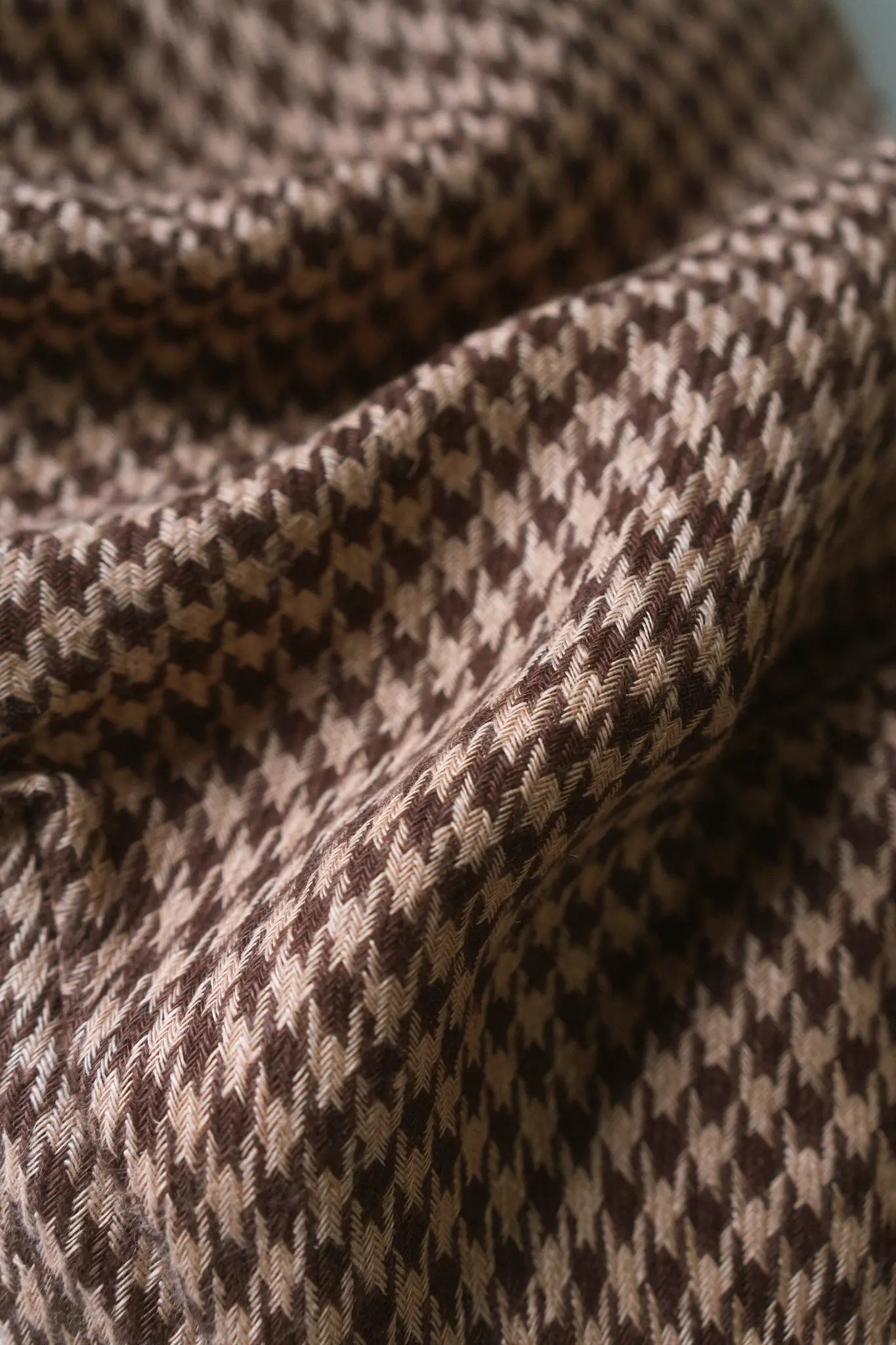 Close detail of handwoven linen in a tan and chocolate houndstooth weave, folded to catch the light
