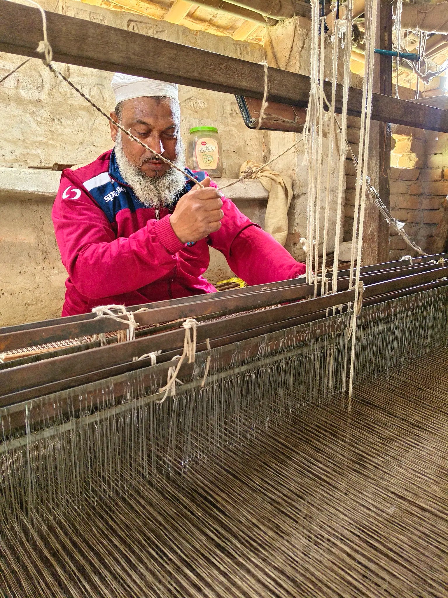 A master handloom weaver threading warp yarns by hand at his wooden loom in a village workshop