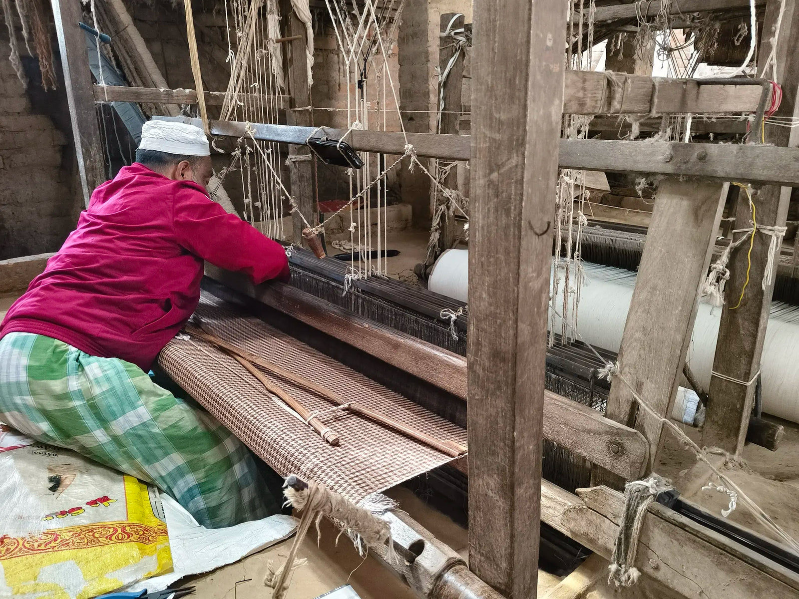 A weaver at his wooden handloom in a village workshop in Eastern India, a length of houndstooth linen on the beam