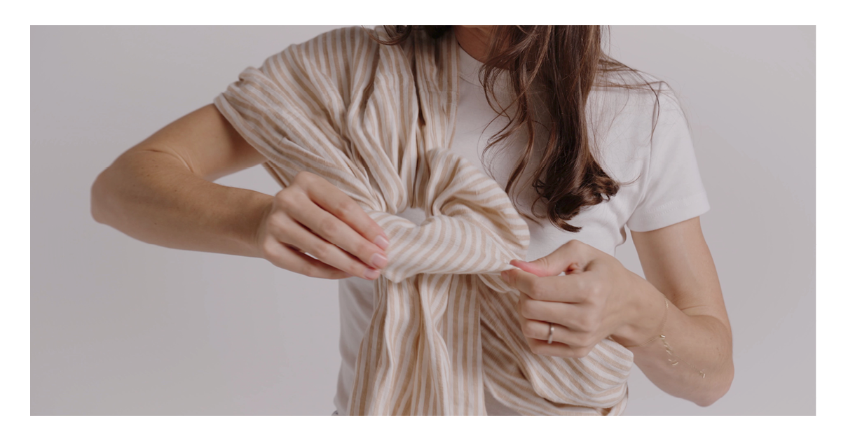 Hands pulling the linen tail back through the rings to seat the Sling Carrier fabric across the chest