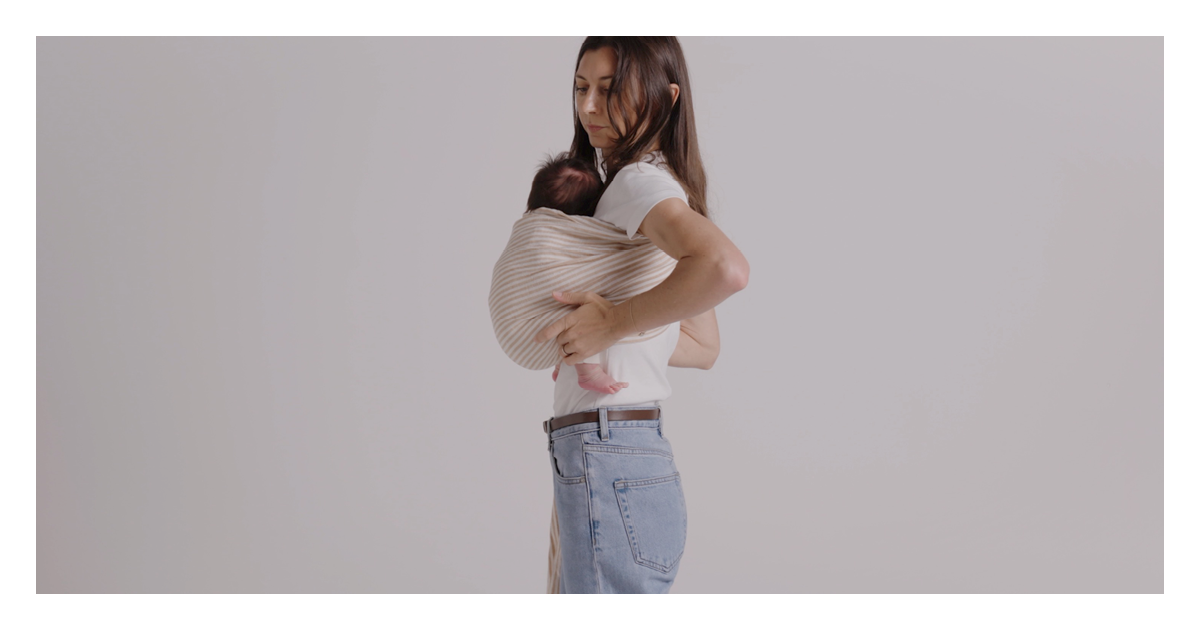 Side view of a newborn settled in the striped linen Sling Carrier, mum's hand resting on her back