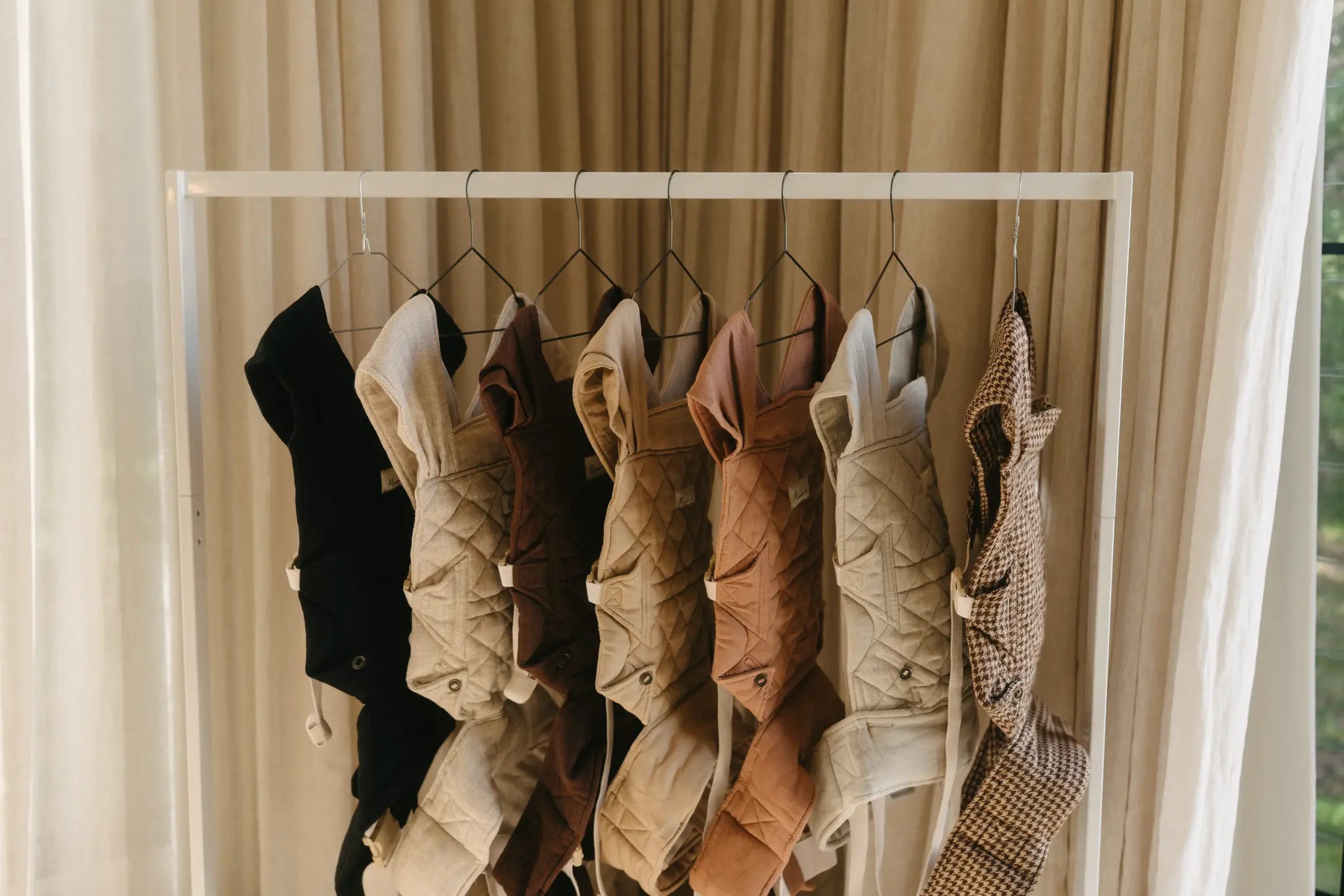 Wide view of the full Daily baby carrier colour range hanging together against a linen curtain