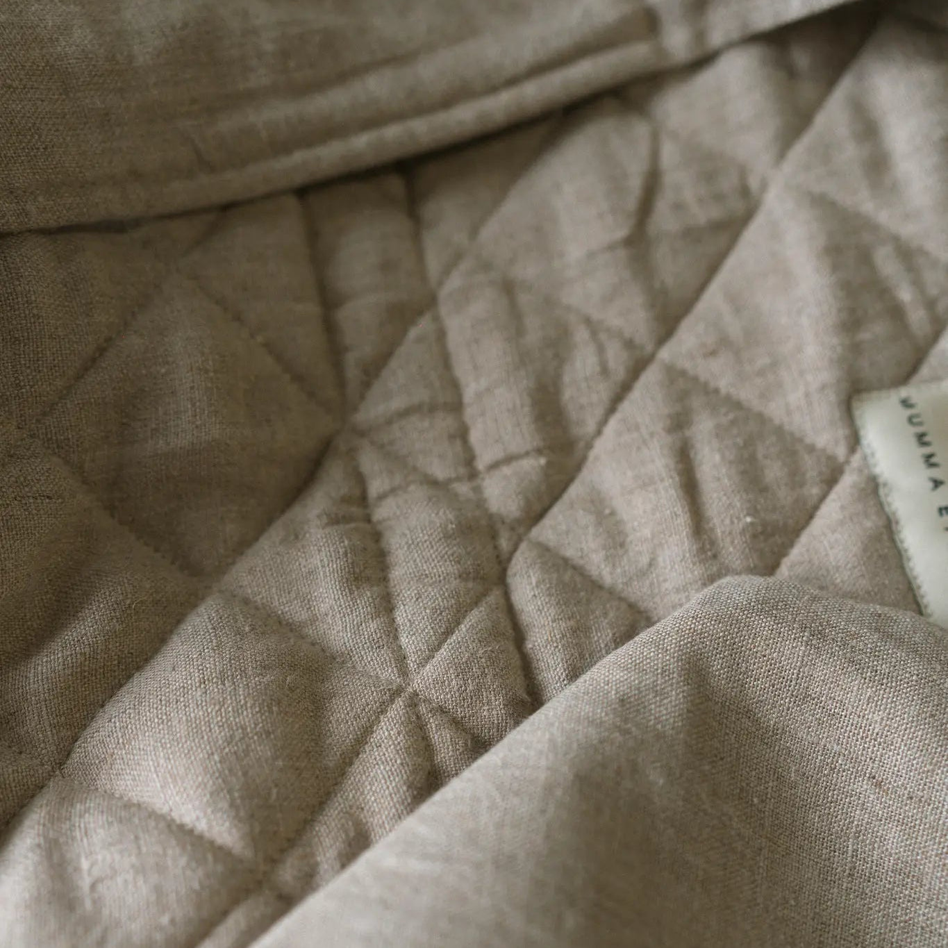 Close on a quilted natural Fleetwood linen panel, the woven brand label just visible at the folded edge