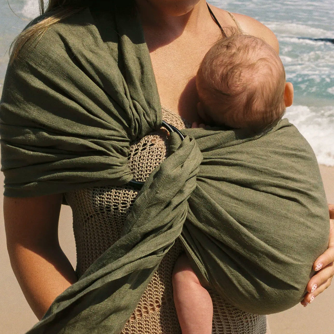 Newborn curled against mum's chest in the Aloe linen Sling baby carrier, rings and tail visible.
