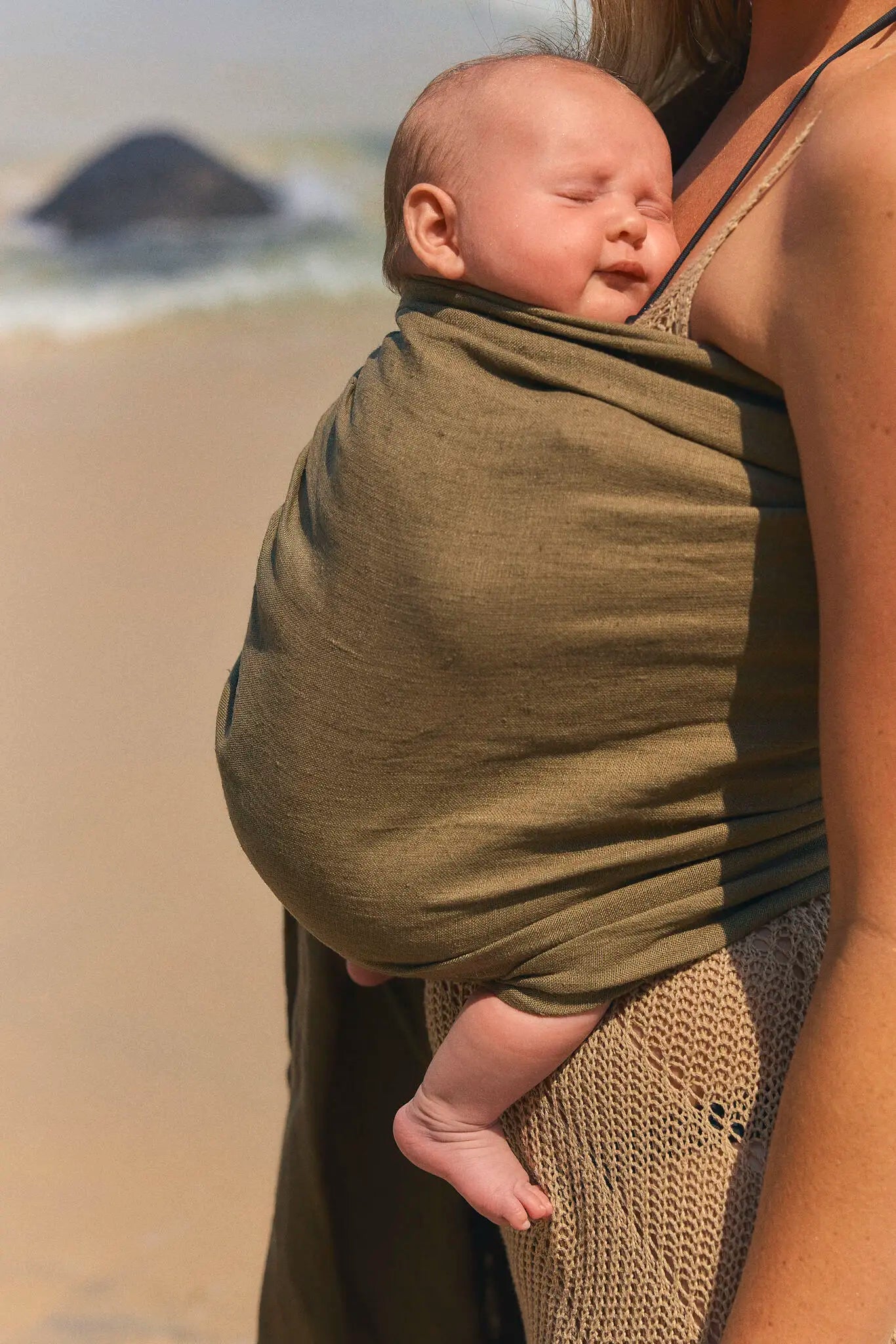 Close view of a sleeping newborn cradled in the olive Aloe linen Sling baby carrier at the beach.