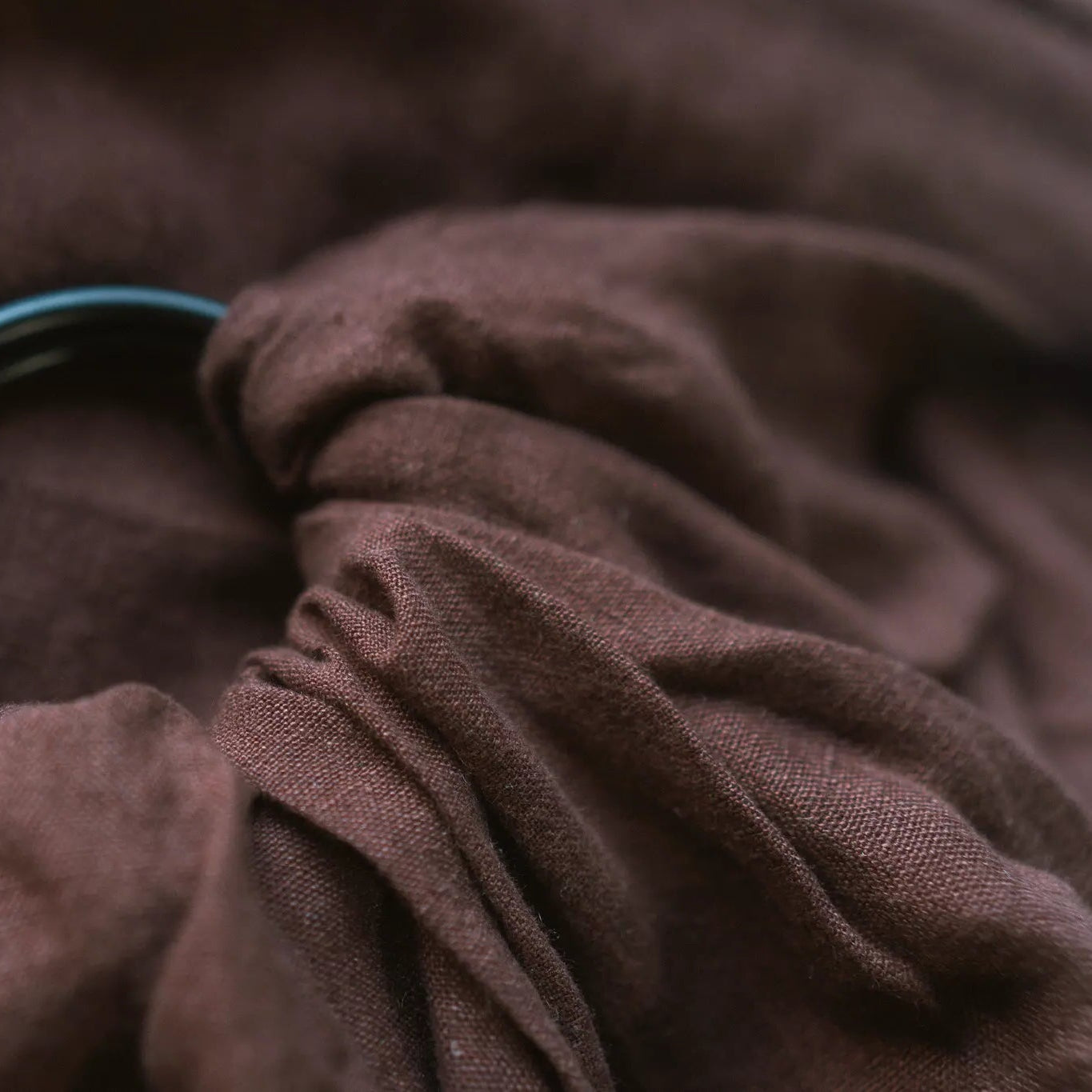 Gathered Coco linen drawn through the twin rings of the Sling carrier, showing how the fabric sits once threaded.