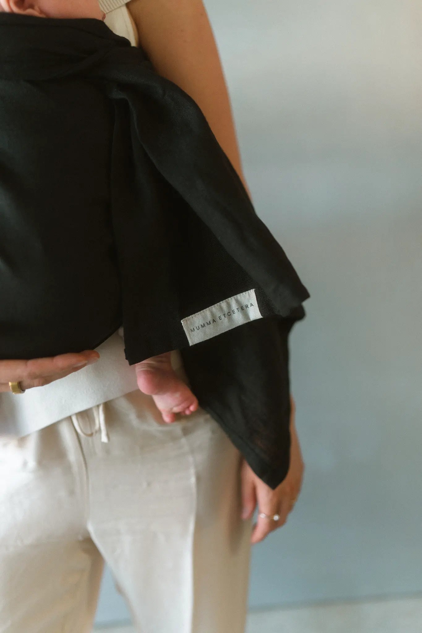 Close view of the Mumma Etcetera label on the Tao linen Sling baby carrier, with a baby's foot showing.