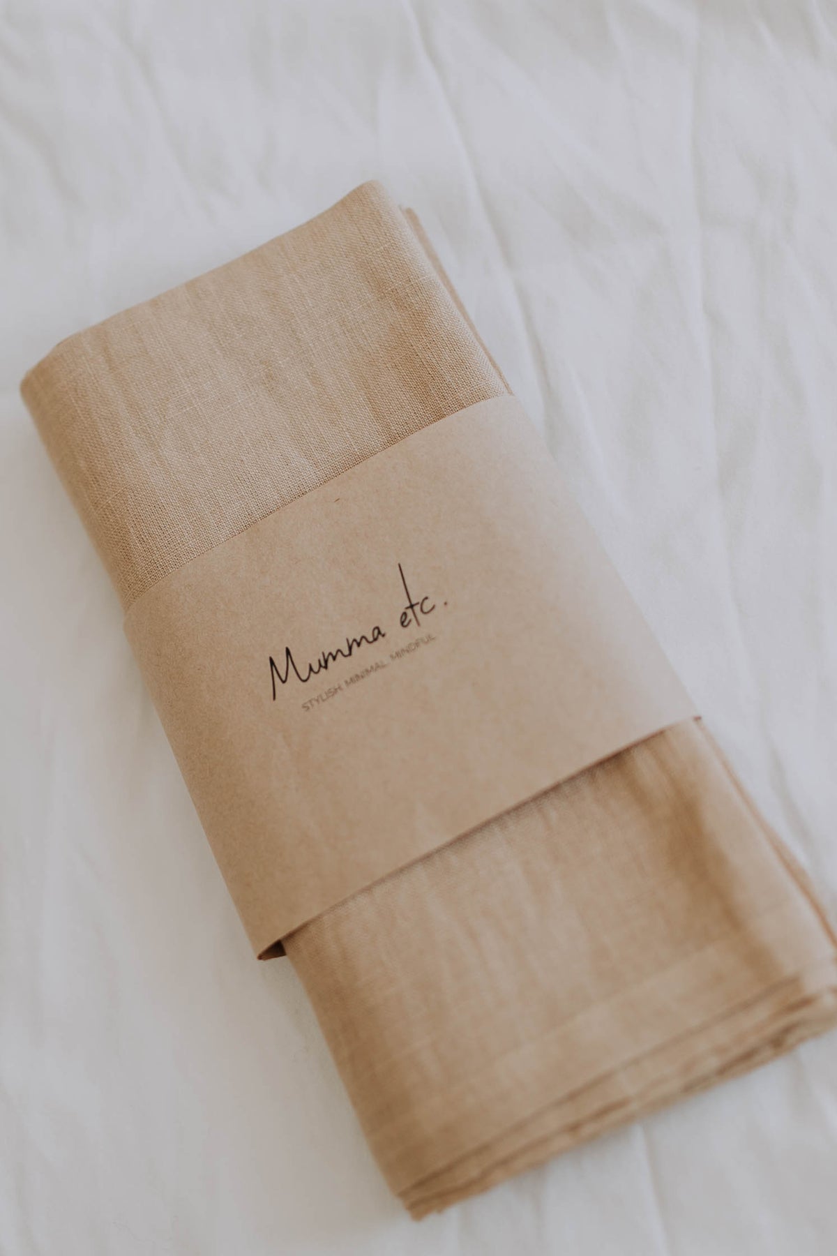 The Bondi linen swaddle folded on a white sheet with its kraft paper Mumma Etcetera band